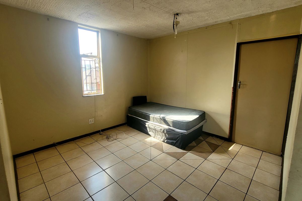 A basic bedroom featuring tiled flooring and a window with security bars, requiring cosmetic updates and ceiling repairs.