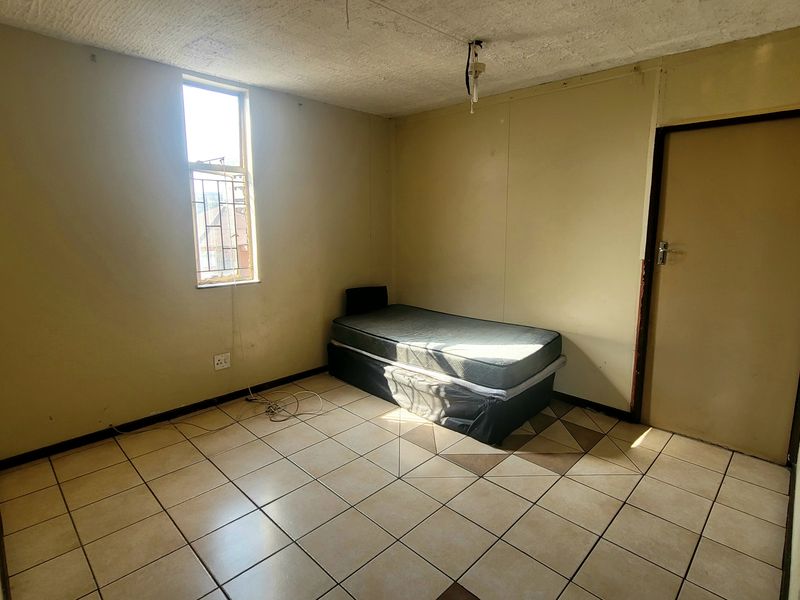 A basic bedroom featuring tiled flooring and a window with security bars, requiring cosmetic updates and ceiling repairs.