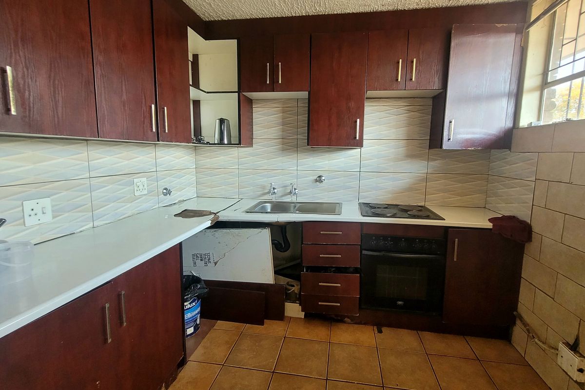 A dated kitchen featuring dark wood cabinetry, a built-in oven and hob, and tiled finishes, currently requiring repairs to the cabinetry and countertop.