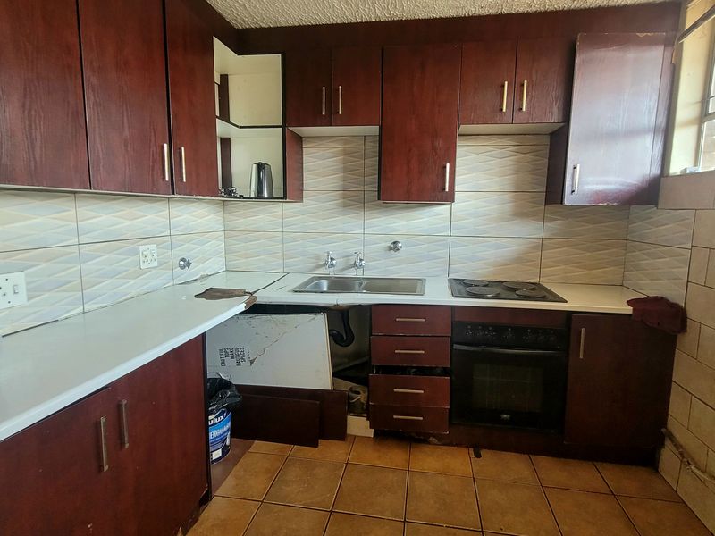 A dated kitchen featuring dark wood cabinetry, a built-in oven and hob, and tiled finishes, currently requiring repairs to the cabinetry and countertop.