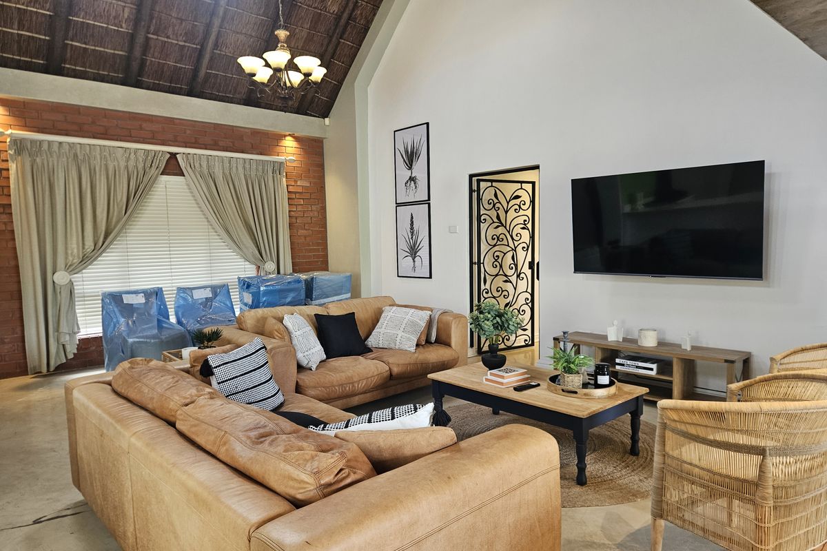 Spacious living room featuring a high vaulted thatched ceiling, exposed brick accent wall, and a decorative wrought iron security gate.