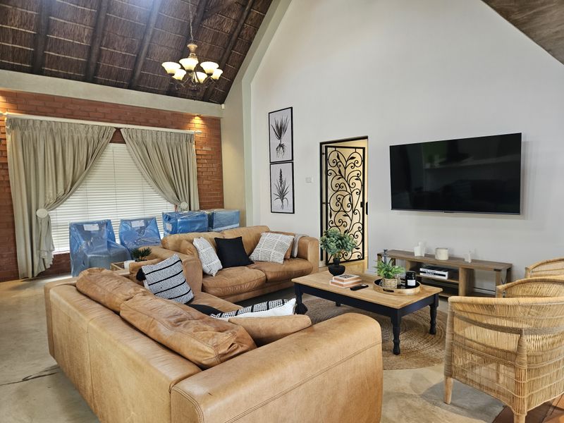 Spacious living room featuring a high vaulted thatched ceiling, exposed brick accent wall, and a decorative wrought iron security gate.