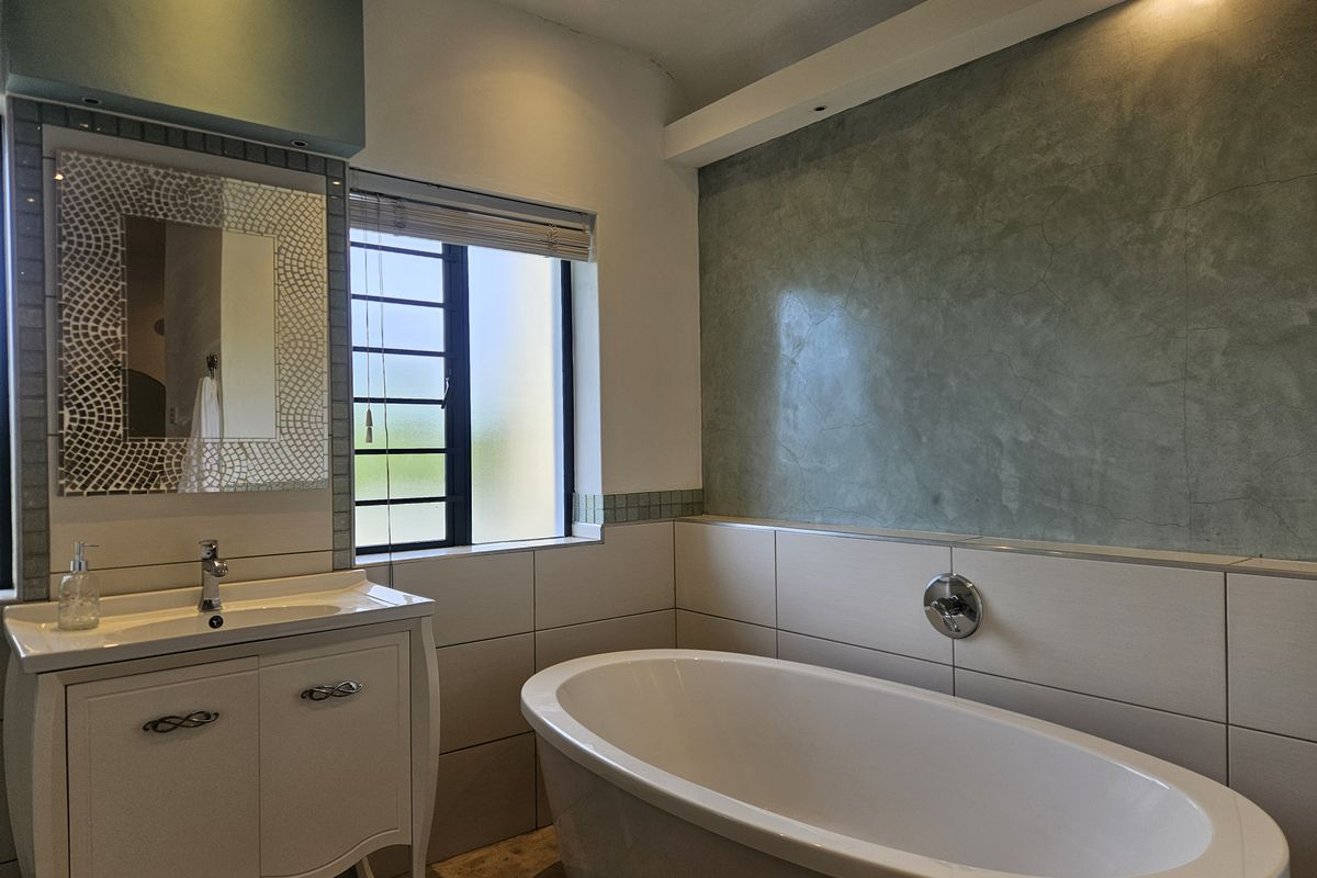 A modern bathroom featuring a sleek freestanding bathtub, a vanity with basin, and a textured feature wall with recessed lighting.