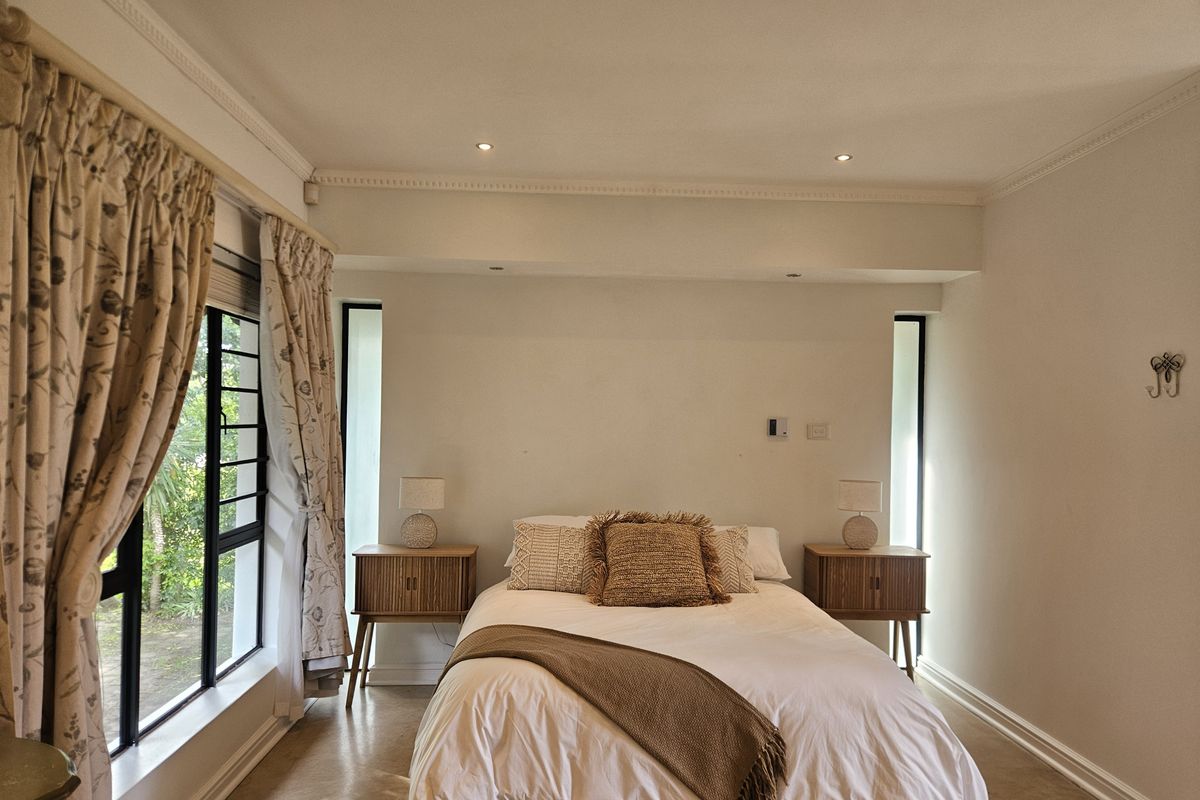 A well-lit bedroom featuring neutral walls, decorative cornicing, and large vertical windows that provide natural light.
