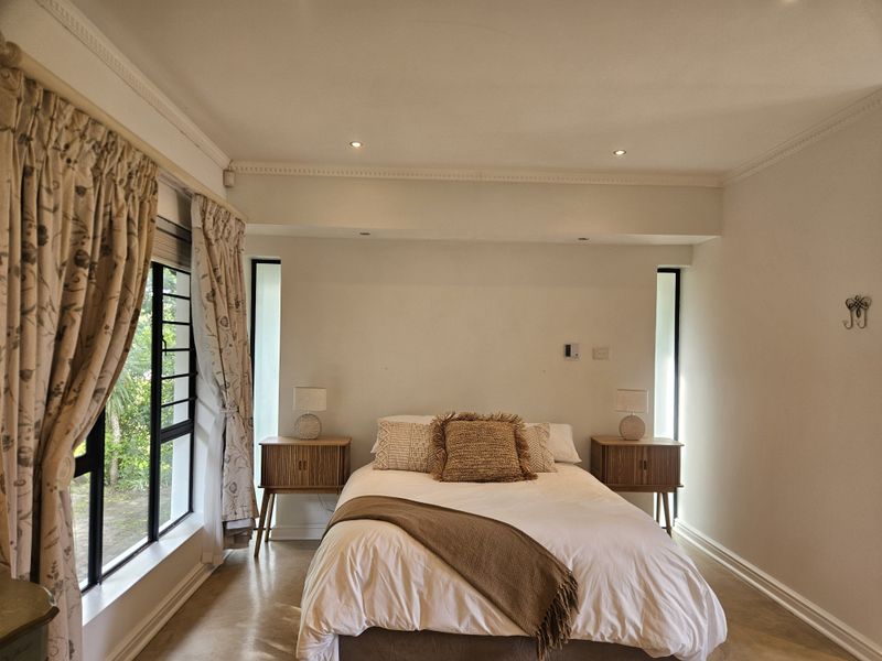 A well-lit bedroom featuring neutral walls, decorative cornicing, and large vertical windows that provide natural light.
