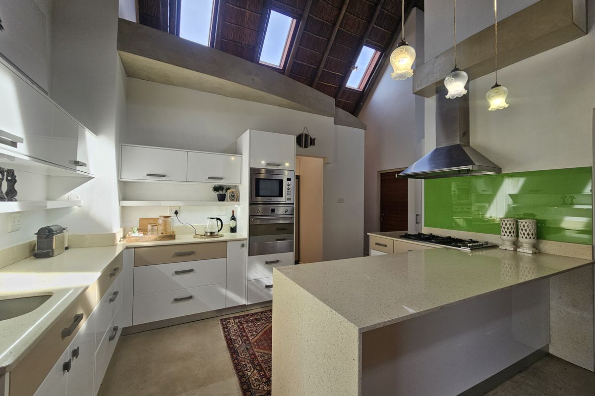 Modern kitchen featuring stone countertops, built-in appliances, a gas hob, and a striking high-vaulted thatched ceiling with integrated skylights.