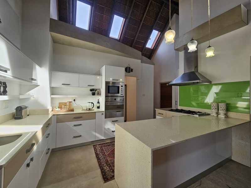 Modern kitchen featuring stone countertops, built-in appliances, a gas hob, and a striking high-vaulted thatched ceiling with integrated skylights.