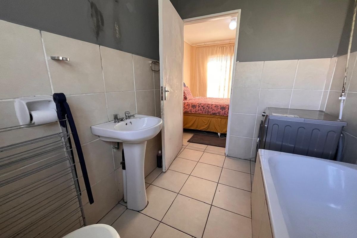 A functional bathroom featuring a pedestal basin, bathtub, and tiled finishes, requiring cosmetic updates to the wall surfaces.