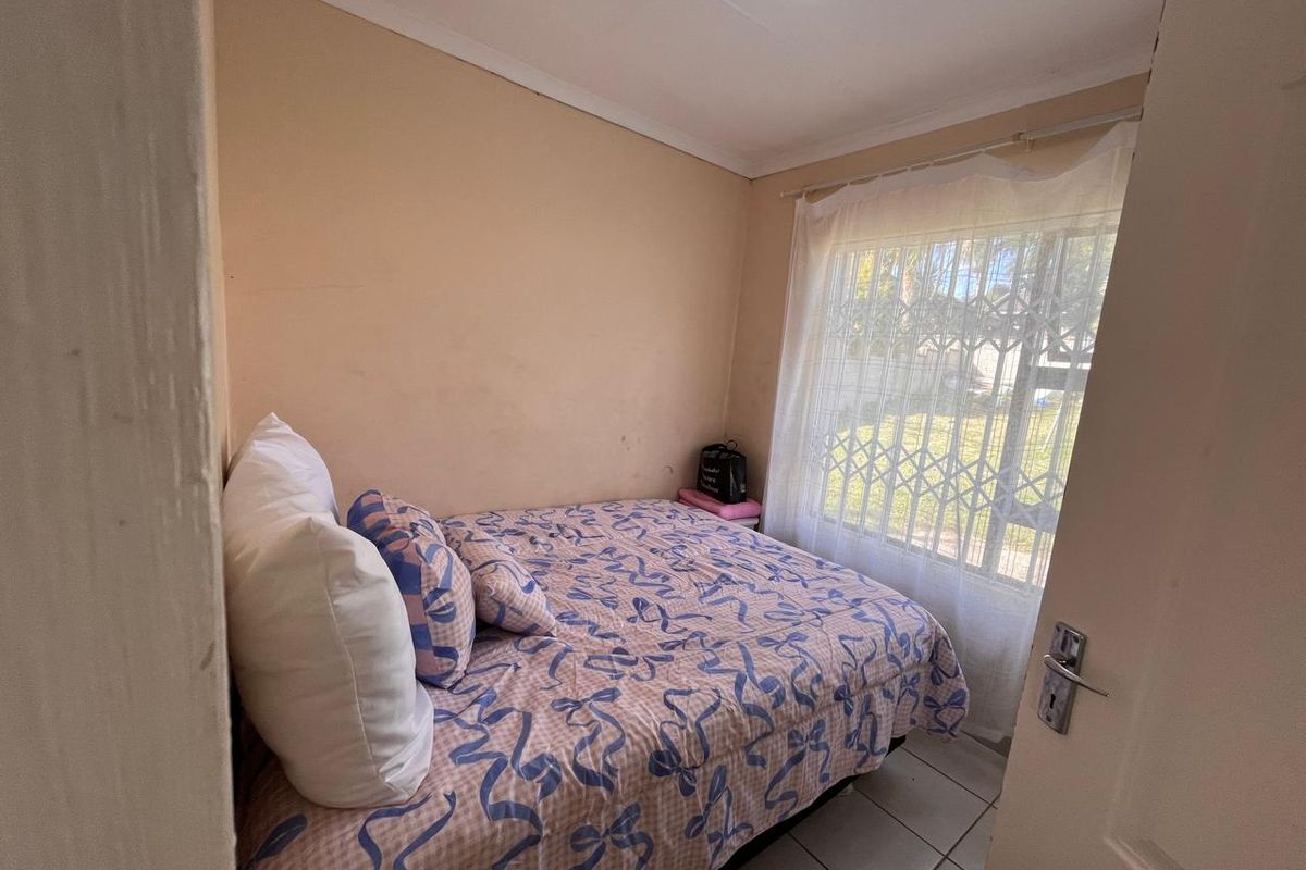 A compact bedroom featuring tiled flooring, a window with a security gate, and neutral wall finishes.
