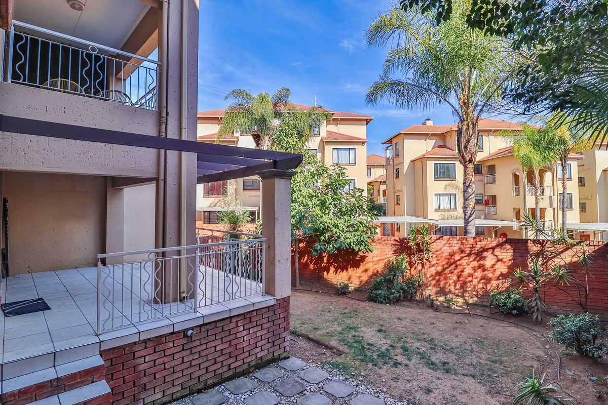 Rear view of the apartment featuring a covered tiled patio with a timber pergola, wrought iron balustrades, and a private garden area.