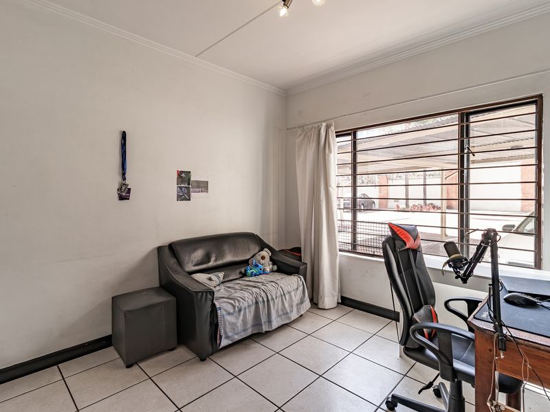 A bedroom featuring tiled flooring and a window fitted with security bars, offering a functional space with potential for cosmetic updates.