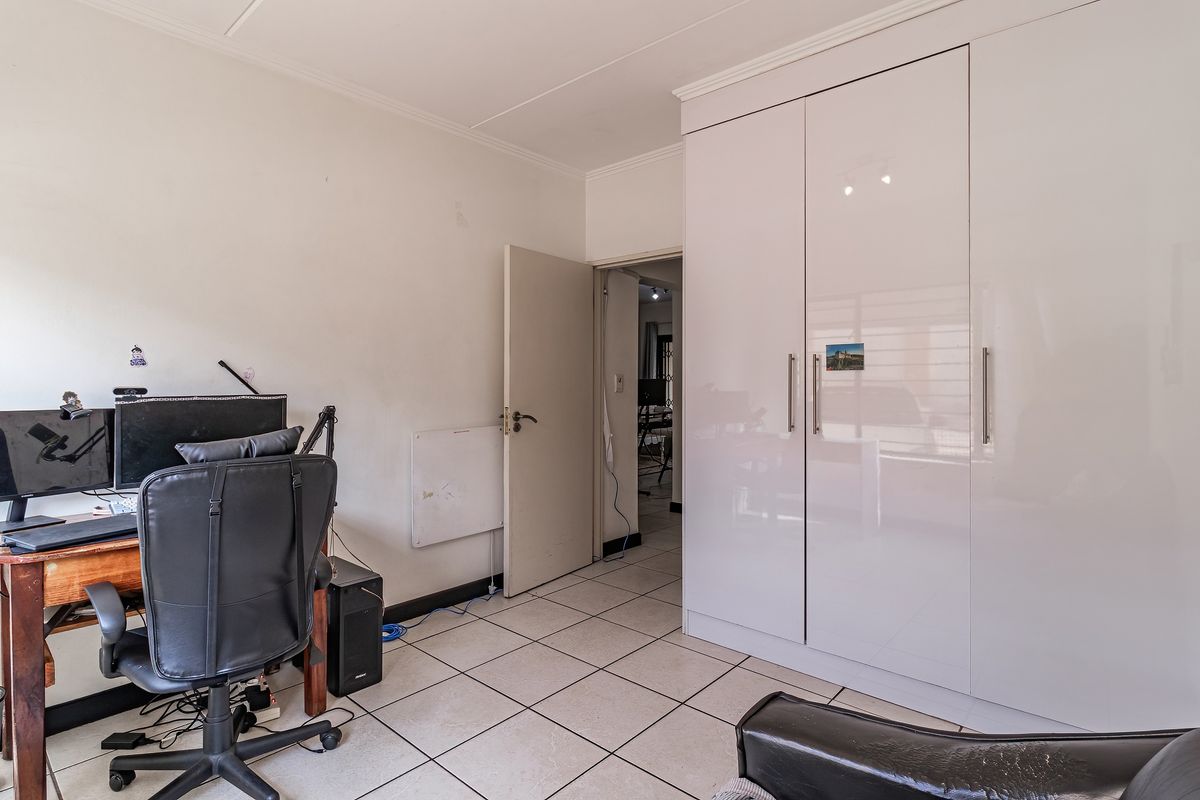 A bedroom featuring tiled flooring and a large, modern white built-in wardrobe with sleek handles.