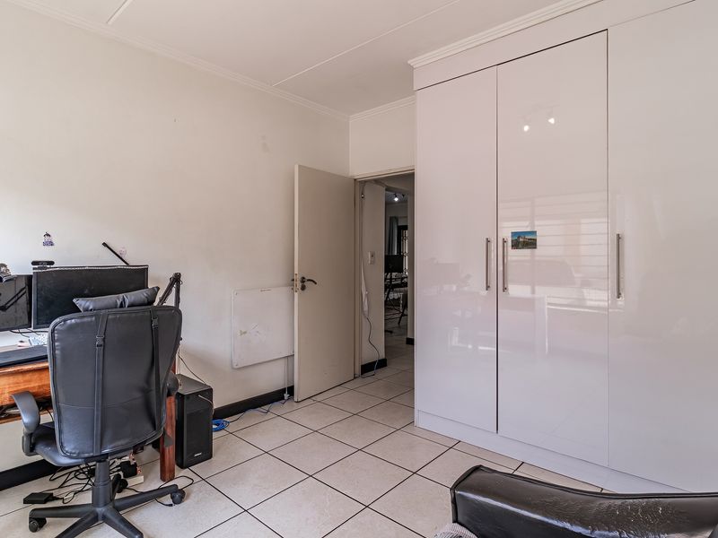 A bedroom featuring tiled flooring and a large, modern white built-in wardrobe with sleek handles.