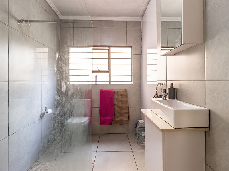 A functional bathroom featuring a glass shower enclosure, a modern vessel sink with vanity storage, and neutral ceramic tiling throughout.