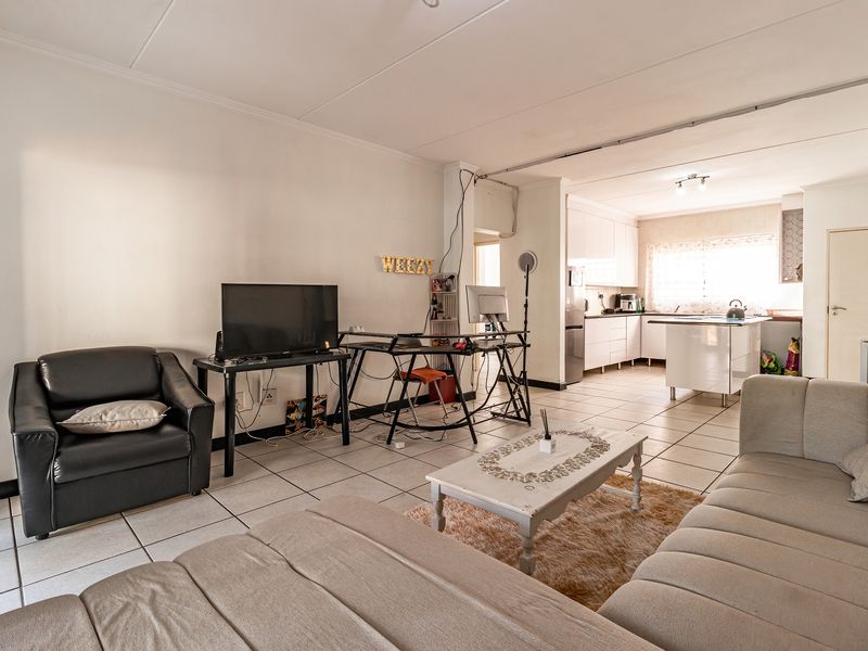 An open-plan living and kitchen area featuring tiled flooring, white cabinetry, and a central kitchen island, offering a functional and connected living space.
