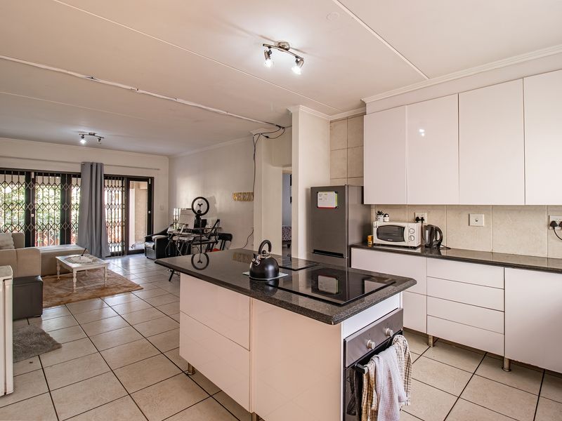 Open-plan living area featuring a modern kitchen with white gloss cabinetry, granite countertops, a central island with a built-in oven, and tiled flooring throughout.
