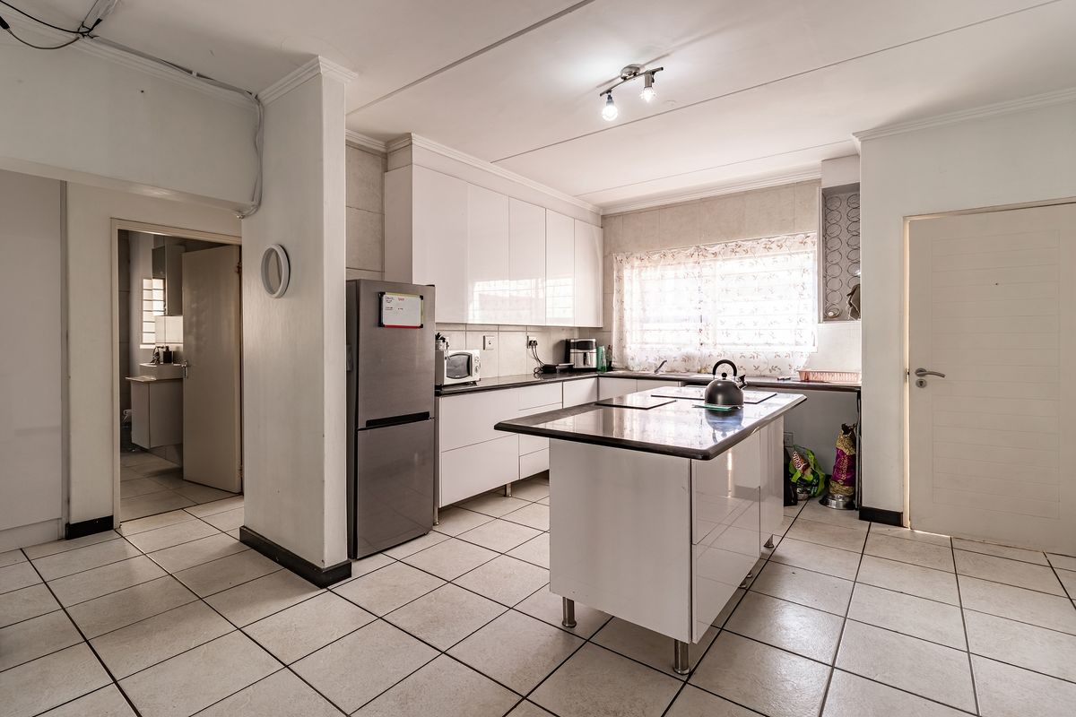 A functional kitchen featuring white cabinetry, a central island with stone countertops, and tiled flooring, with an adjacent view into a bathroom area.