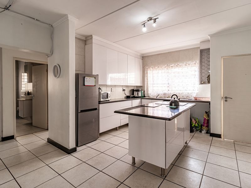 A functional kitchen featuring white cabinetry, a central island with stone countertops, and tiled flooring, with an adjacent view into a bathroom area.