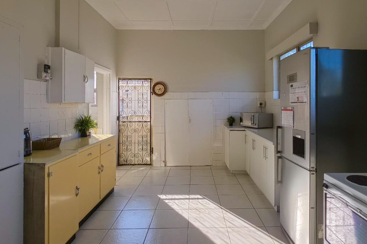 A functional kitchen featuring tiled flooring, built-in cabinetry, and a security gate leading to the exterior, offering potential for modernization.