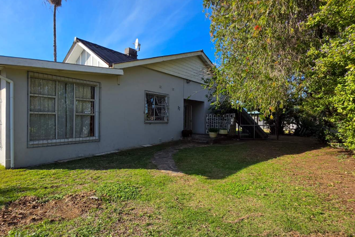 Rear view of the property featuring a metal roof, security bars on windows, and a garden area with a concrete pathway.