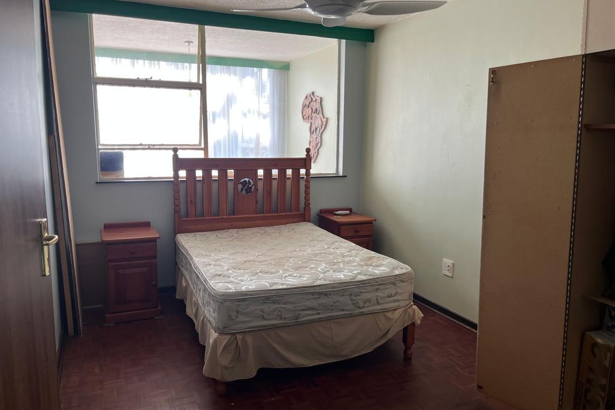 A bedroom featuring parquet flooring, a ceiling fan, and a built-in cupboard, offering a functional space with potential for cosmetic updates.