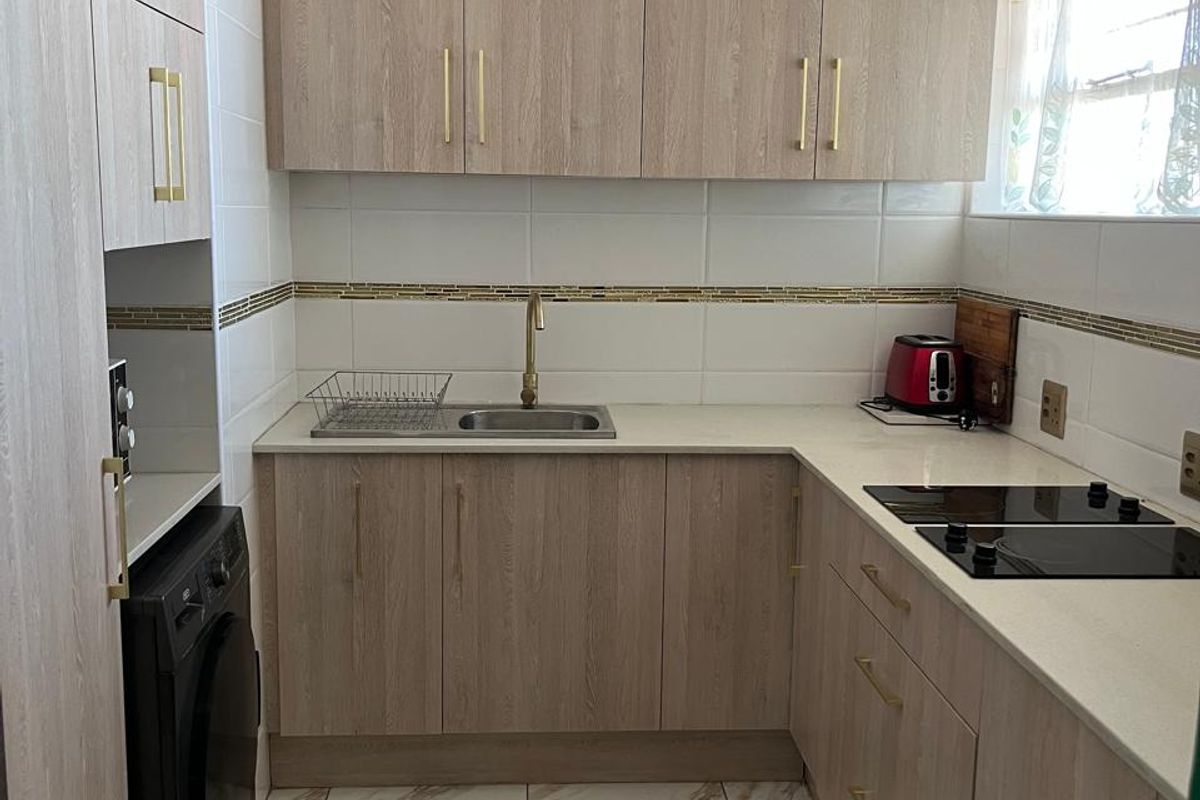 A modern, well-maintained kitchen featuring light wood-grain cabinetry, stone countertops, brass hardware, and marble-look floor tiles with an integrated induction hob.
