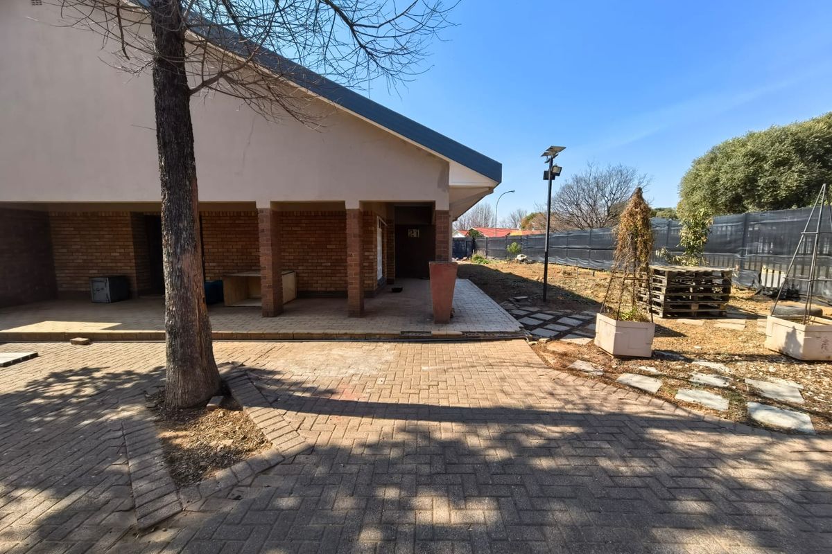 Rear exterior view of the house featuring a covered patio area, brick paving, and a spacious garden space with a solar light pole.