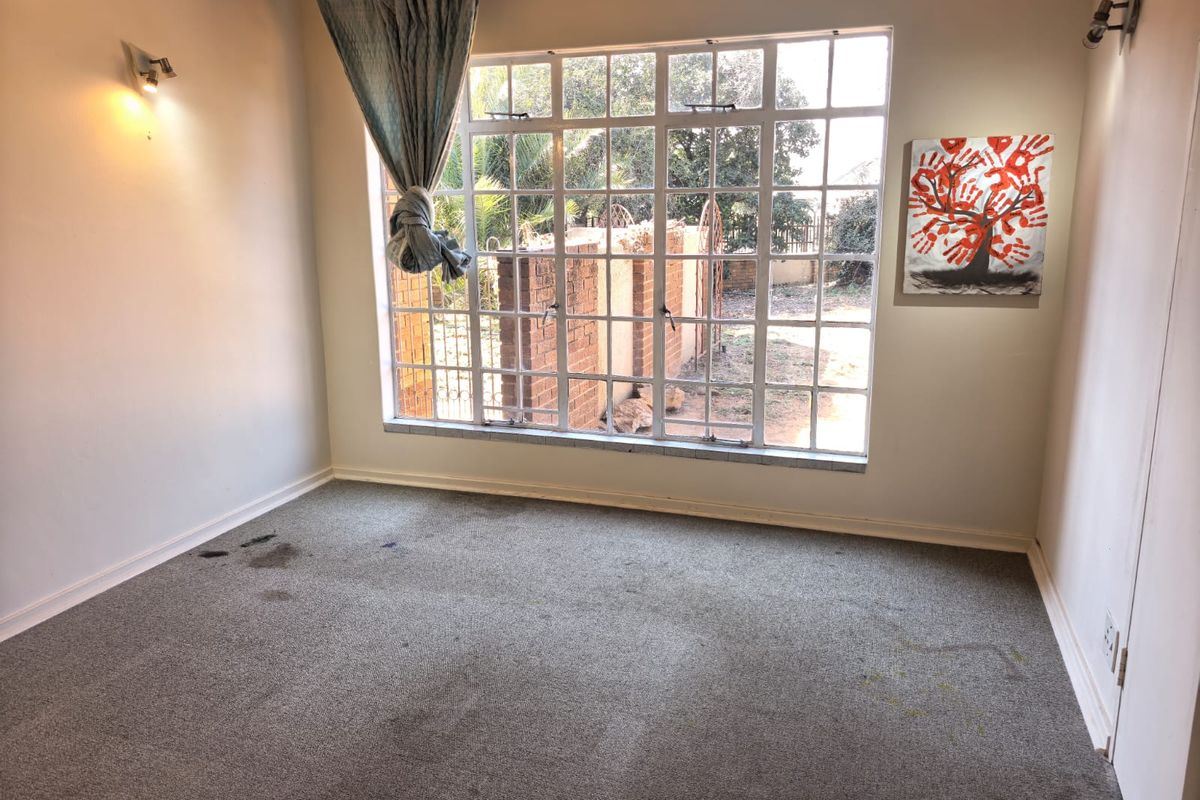 An empty bedroom featuring a large grid-pattern window, wall-mounted lighting, and carpeted flooring in need of replacement.