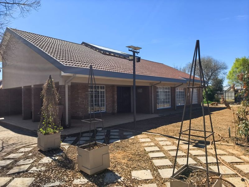 Front view of a single-story brick house featuring a tiled roof, solar panels, and a paved garden area.