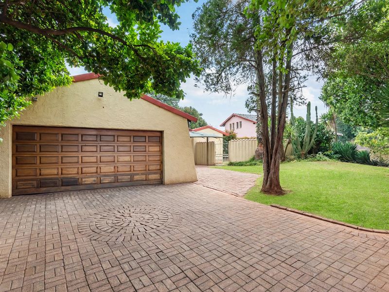 Front exterior view featuring a paved driveway, a wooden garage door, and a well-maintained garden area.