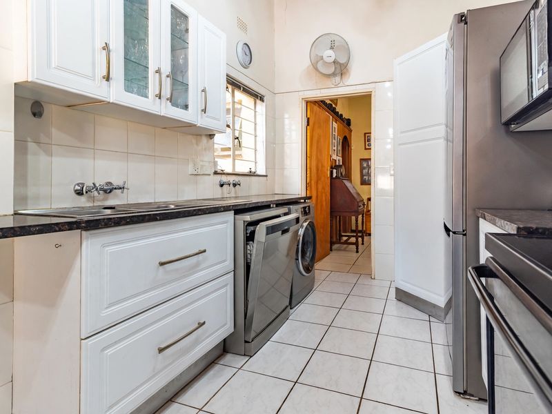 A functional kitchen featuring white cabinetry, dark laminate countertops, tiled splashbacks, and tiled flooring, with integrated space for laundry appliances.