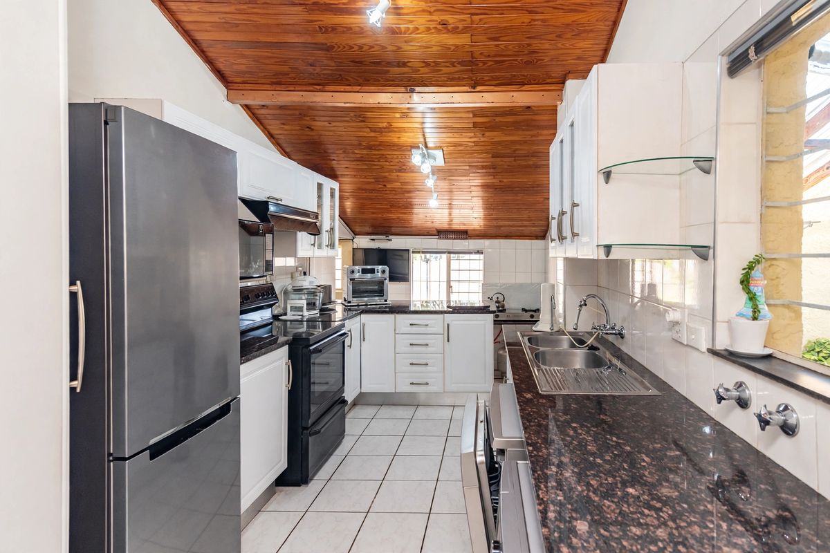 A functional kitchen featuring granite countertops, a double bowl stainless steel sink, white cabinetry, and a distinctive timber tongue and groove ceiling.