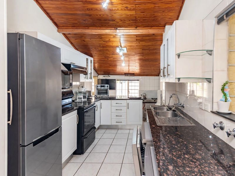 A functional kitchen featuring granite countertops, a double bowl stainless steel sink, white cabinetry, and a distinctive timber tongue and groove ceiling.