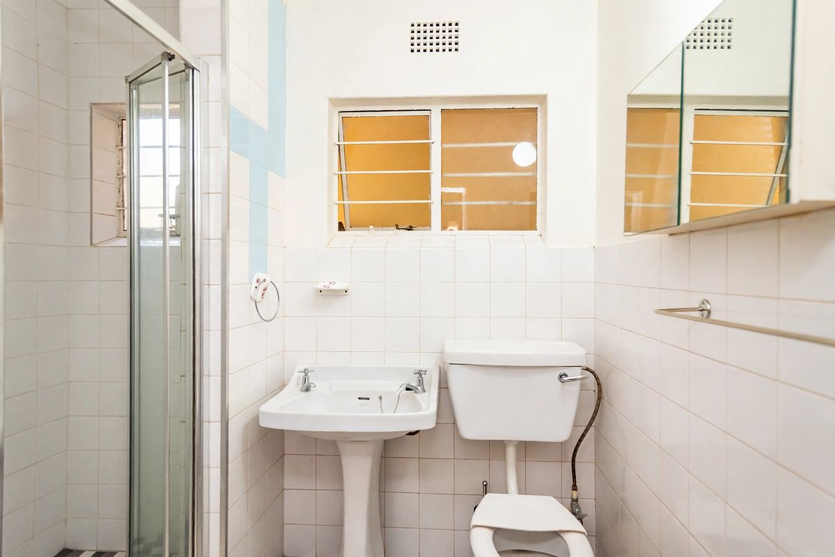 A functional bathroom featuring a pedestal basin, toilet, and shower enclosure with white wall tiling and a built-in medicine cabinet.
