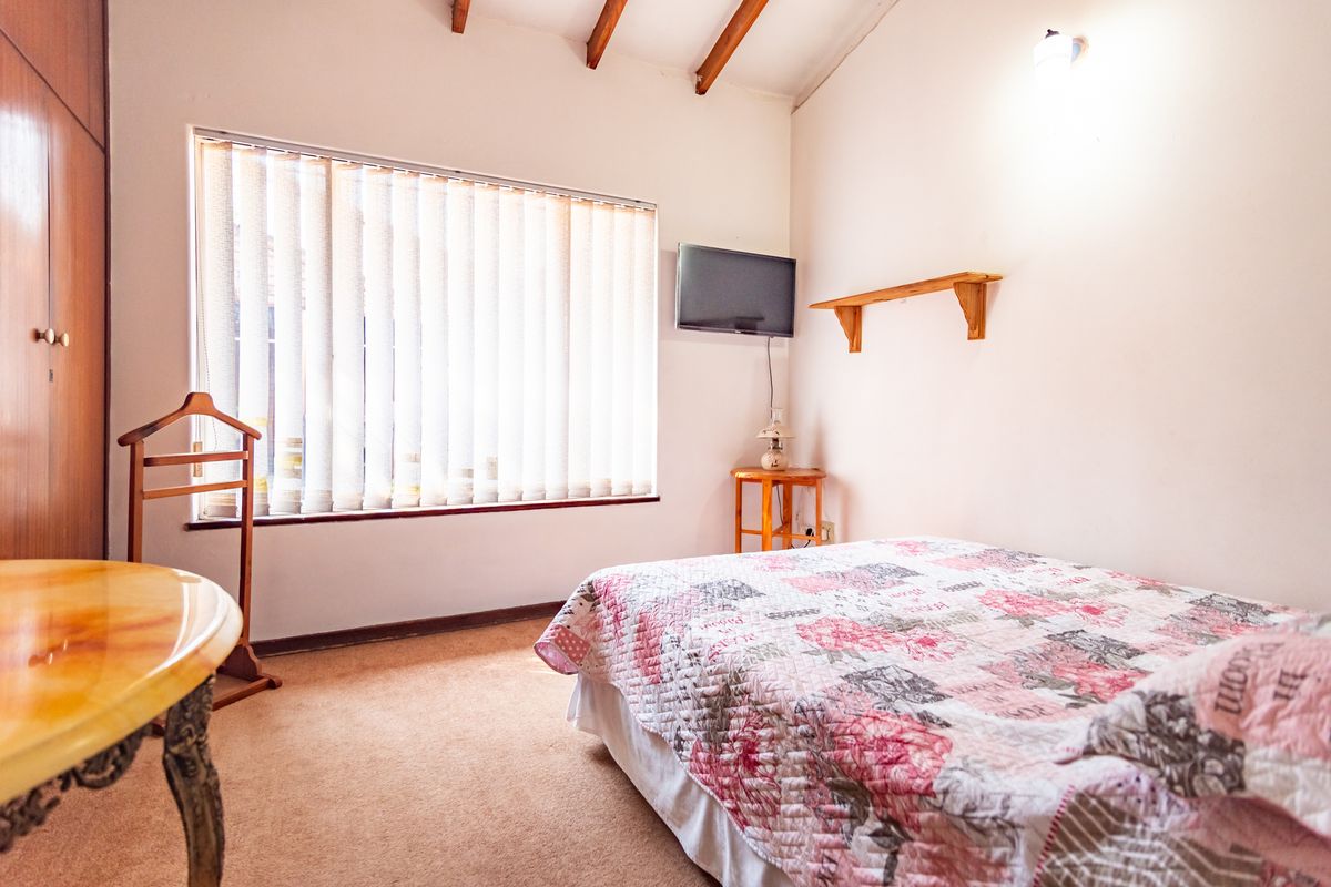 A bedroom featuring exposed timber rafters, built-in wardrobe storage, and a large window with vertical blinds.