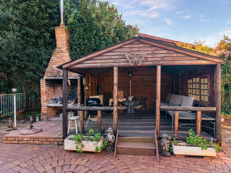 A rustic timber gazebo featuring an integrated brick fireplace and outdoor patio area, set within a paved garden space.