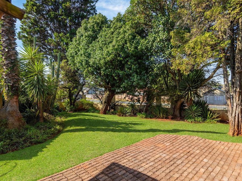 A well-maintained private garden featuring a brick-paved patio area, lush green lawn, and mature trees providing shade and privacy.