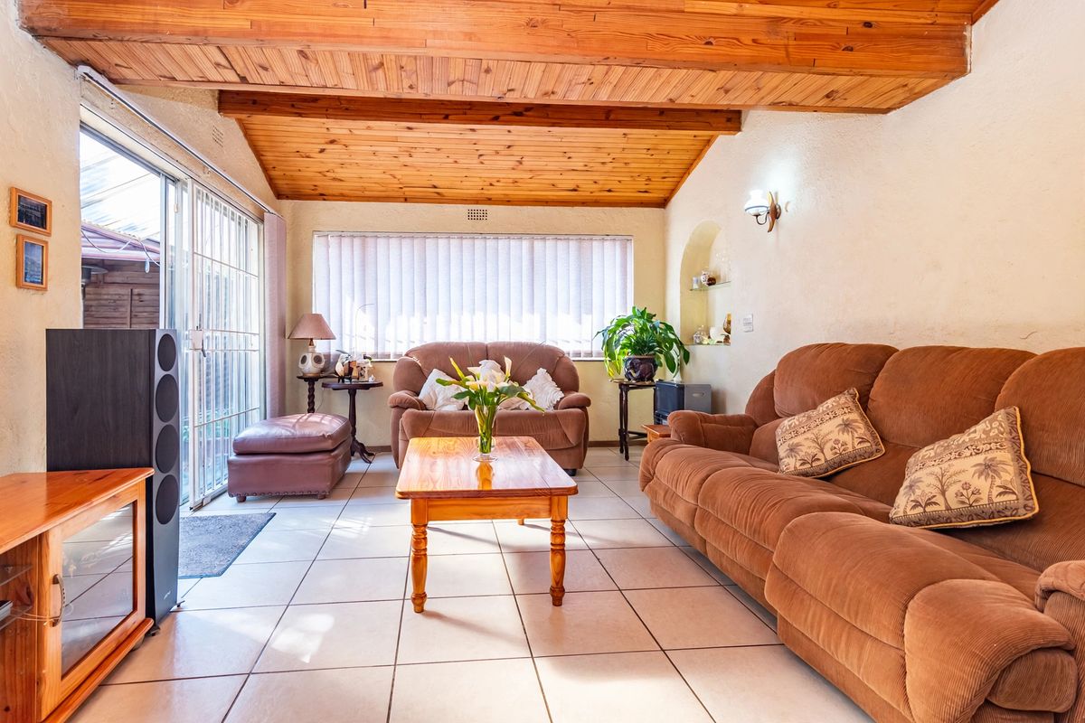 A living room featuring a vaulted timber ceiling, tiled flooring, and a sliding glass door providing access to the exterior.