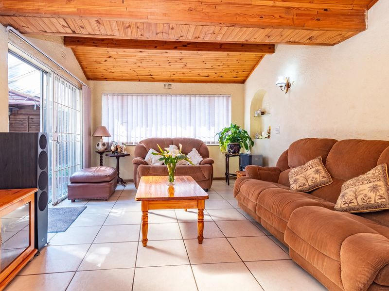 A living room featuring a vaulted timber ceiling, tiled flooring, and a sliding glass door providing access to the exterior.