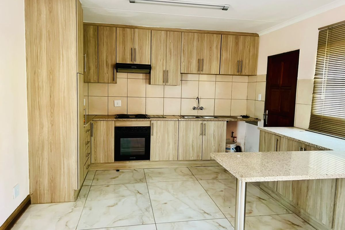A functional kitchen featuring light wood-grain cabinetry, granite countertops, built-in oven, hob, extractor fan, and tiled flooring.