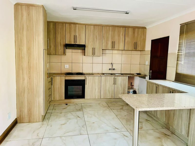 A functional kitchen featuring light wood-grain cabinetry, granite countertops, built-in oven, hob, extractor fan, and tiled flooring.