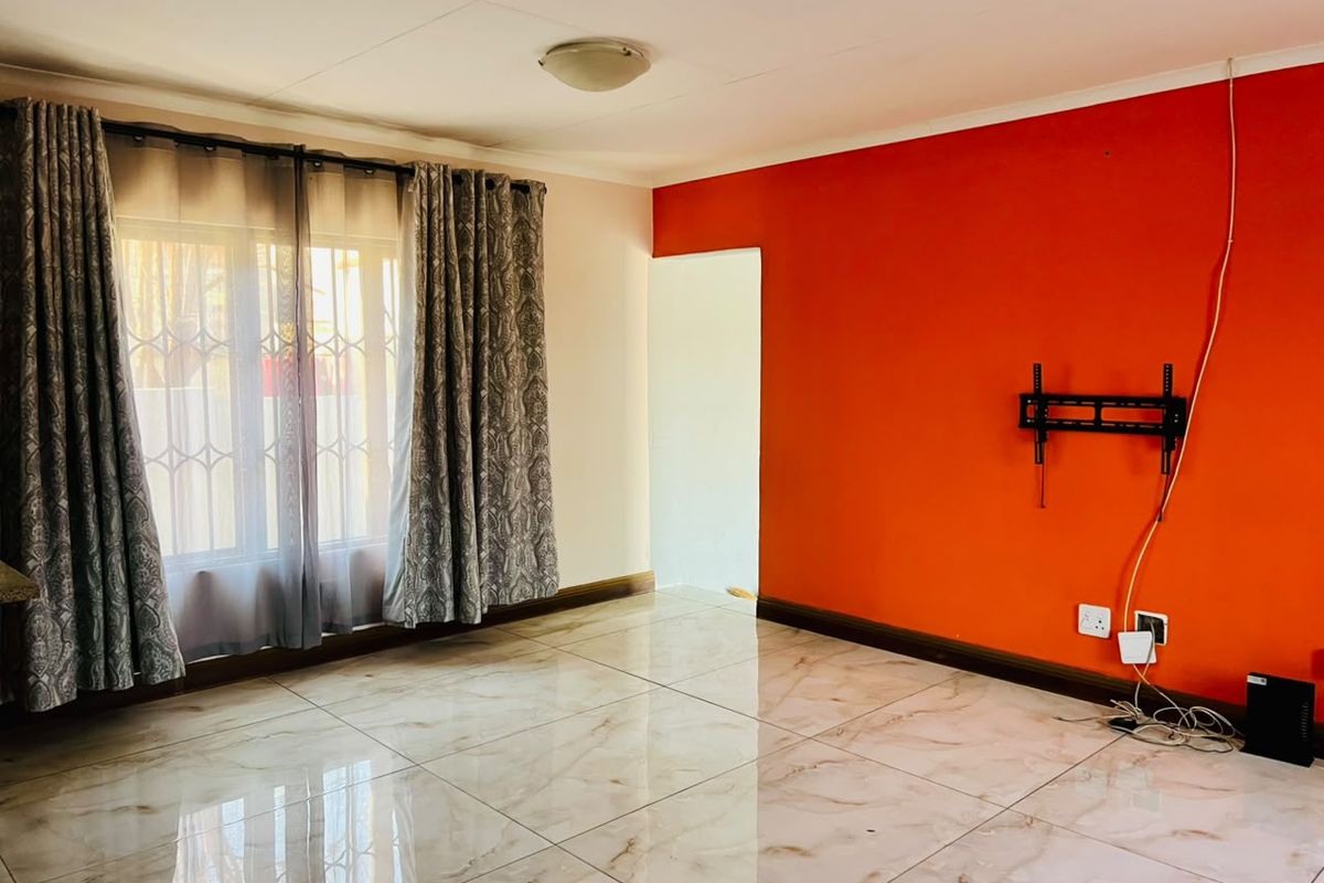 A bright, empty living room featuring polished marble-look floor tiles, a bold red accent wall, and a wall-mounted television bracket.