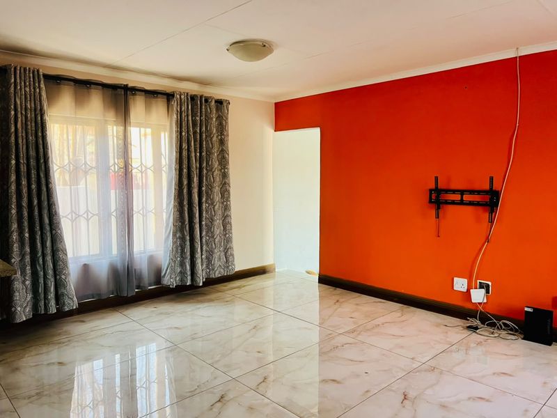 A bright, empty living room featuring polished marble-look floor tiles, a bold red accent wall, and a wall-mounted television bracket.