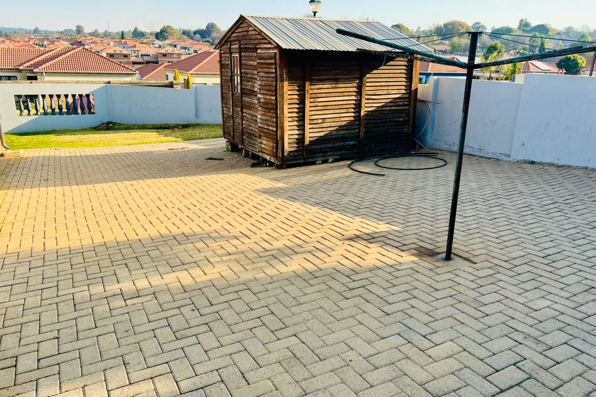 A paved rear patio area featuring a wooden garden shed, perimeter walling, and a rotary clothesline, offering potential for outdoor entertainment space.