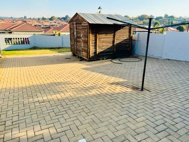 A paved rear patio area featuring a wooden garden shed, perimeter walling, and a rotary clothesline, offering potential for outdoor entertainment space.