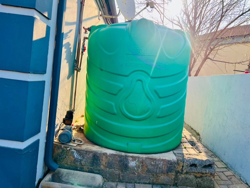 Exterior utility area featuring a 2500L water storage tank and pump system installed on a raised brick plinth.