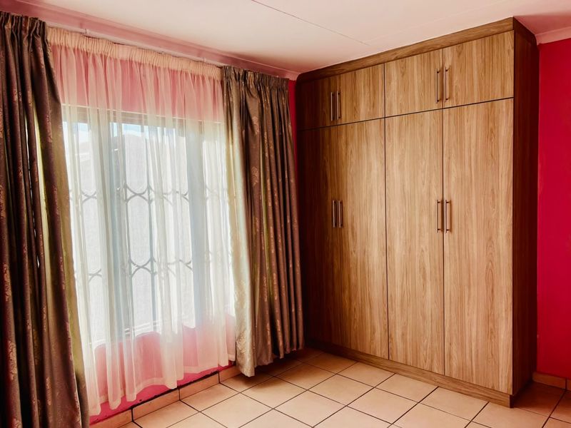 A bedroom featuring built-in wooden cupboards, tiled flooring, and security bars on the window.