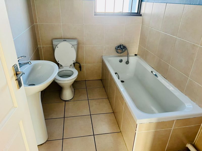 A functional bathroom featuring a pedestal basin, toilet, and bathtub with neutral wall and floor tiling.