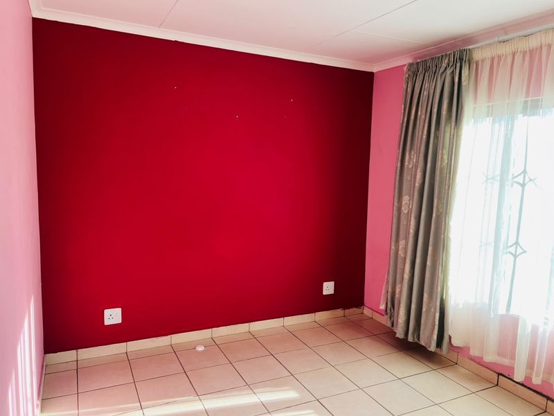 An empty bedroom featuring ceramic tiled flooring and a window with a security gate, ready for a fresh coat of paint.