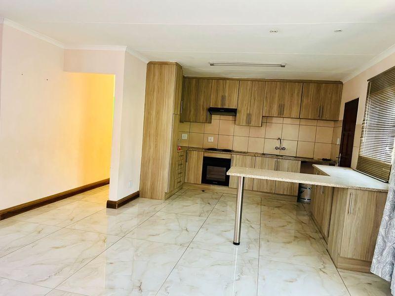 A clean, modern kitchen featuring light wood-finish cabinetry, built-in oven, extractor fan, and a breakfast bar with tiled flooring throughout.